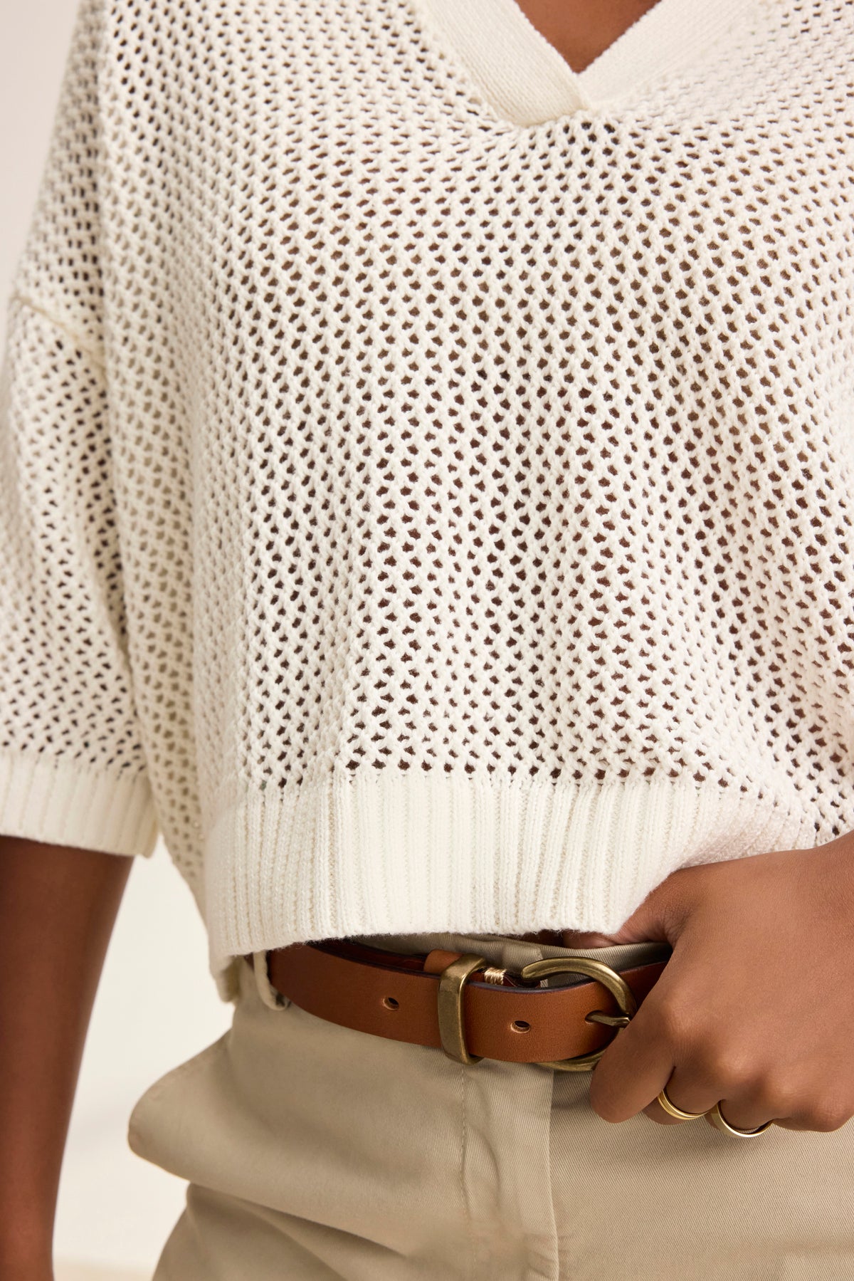 A person stands casually with one hand on their hip, wearing a YORK COTTON CASHMERE MESH SWEATER POLO by Velvet by Jenny Graham, paired with beige pants and a brown belt.-38928816210113