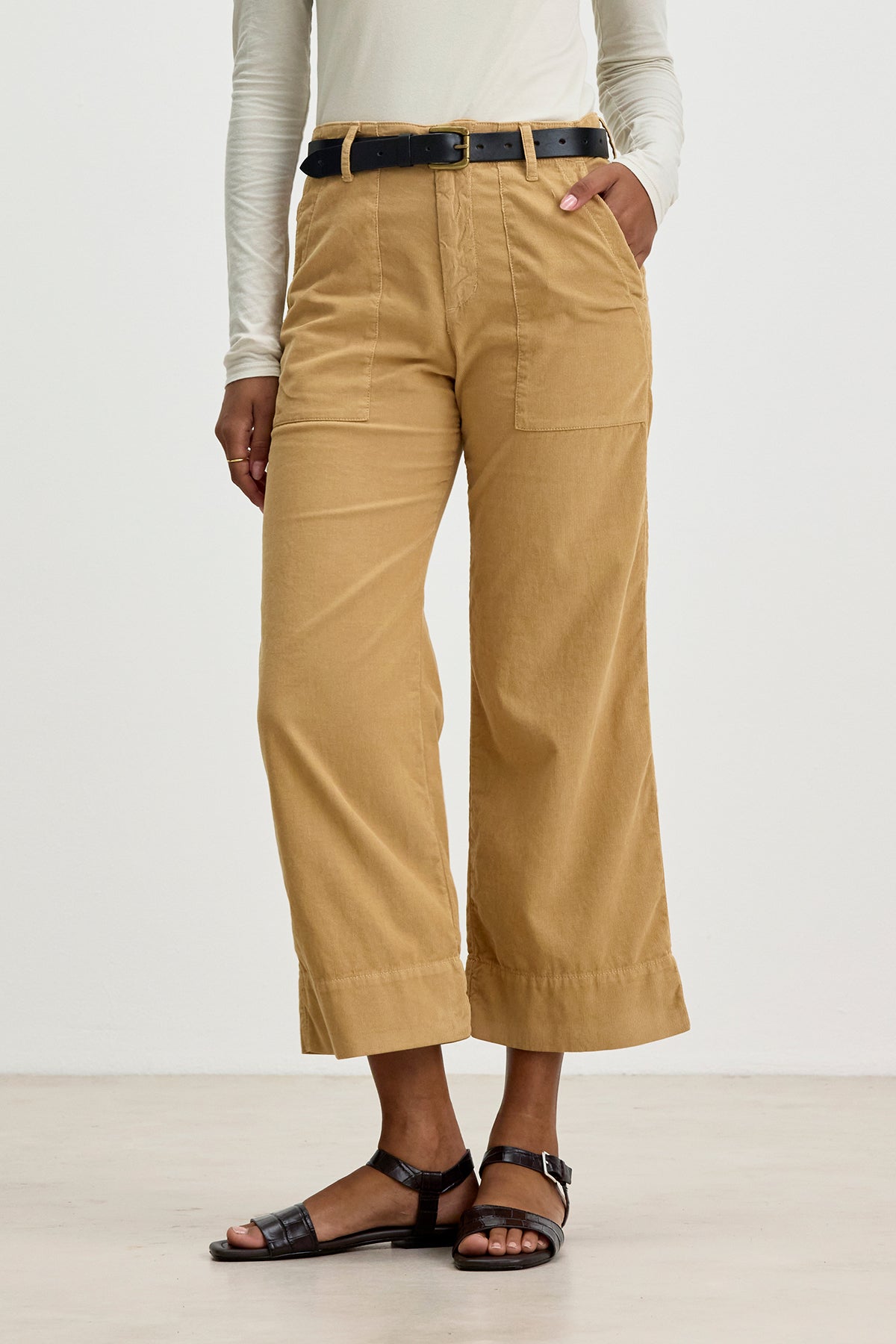 A person wearing a long-sleeve white top, Velvet by Graham & Spencer VERA CORDUROY PANT in beige with pockets, a black belt, and black sandals.-37855966396609