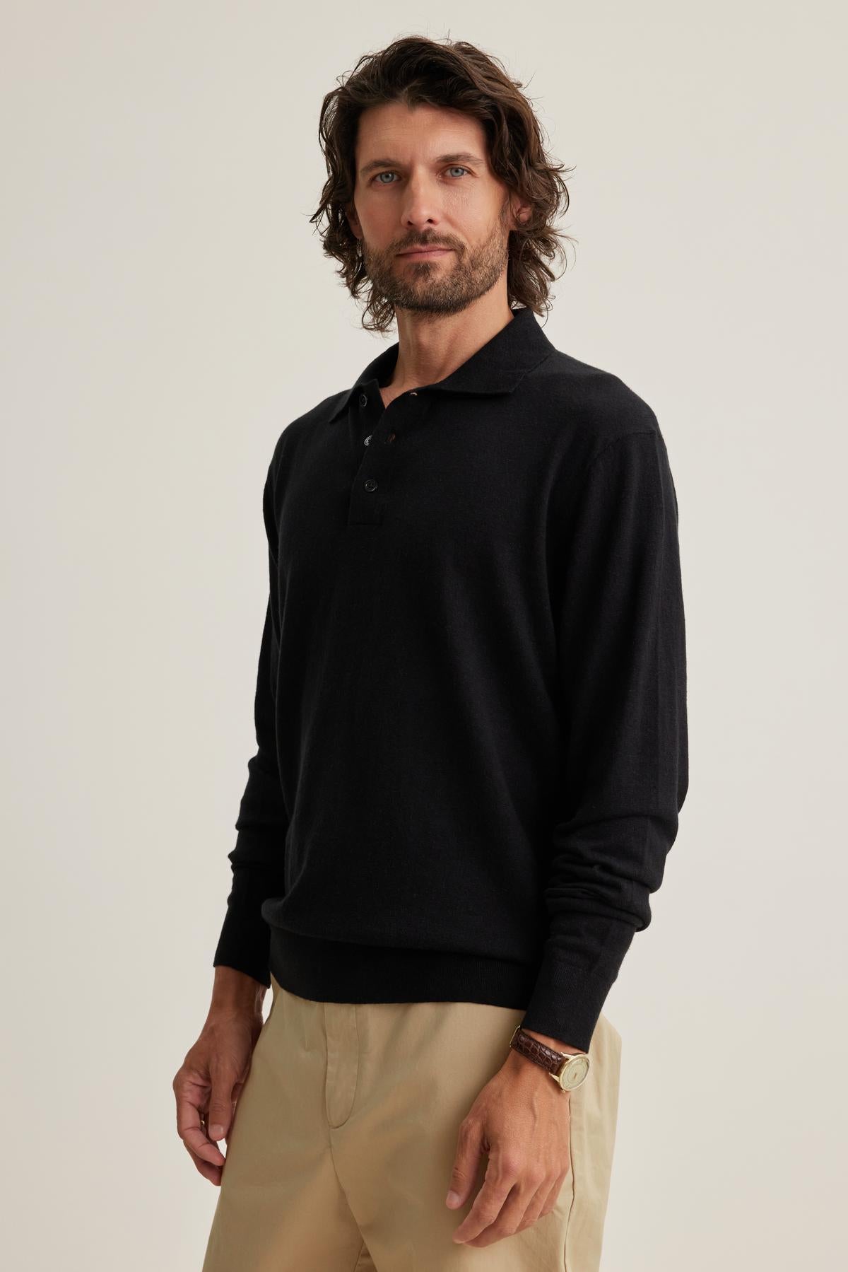 A man with shoulder-length hair wears a black MATTEO COTTON LINEN SWEATER POLO from Velvet by Graham & Spencer and beige pants, standing against a plain background.-38643324780737