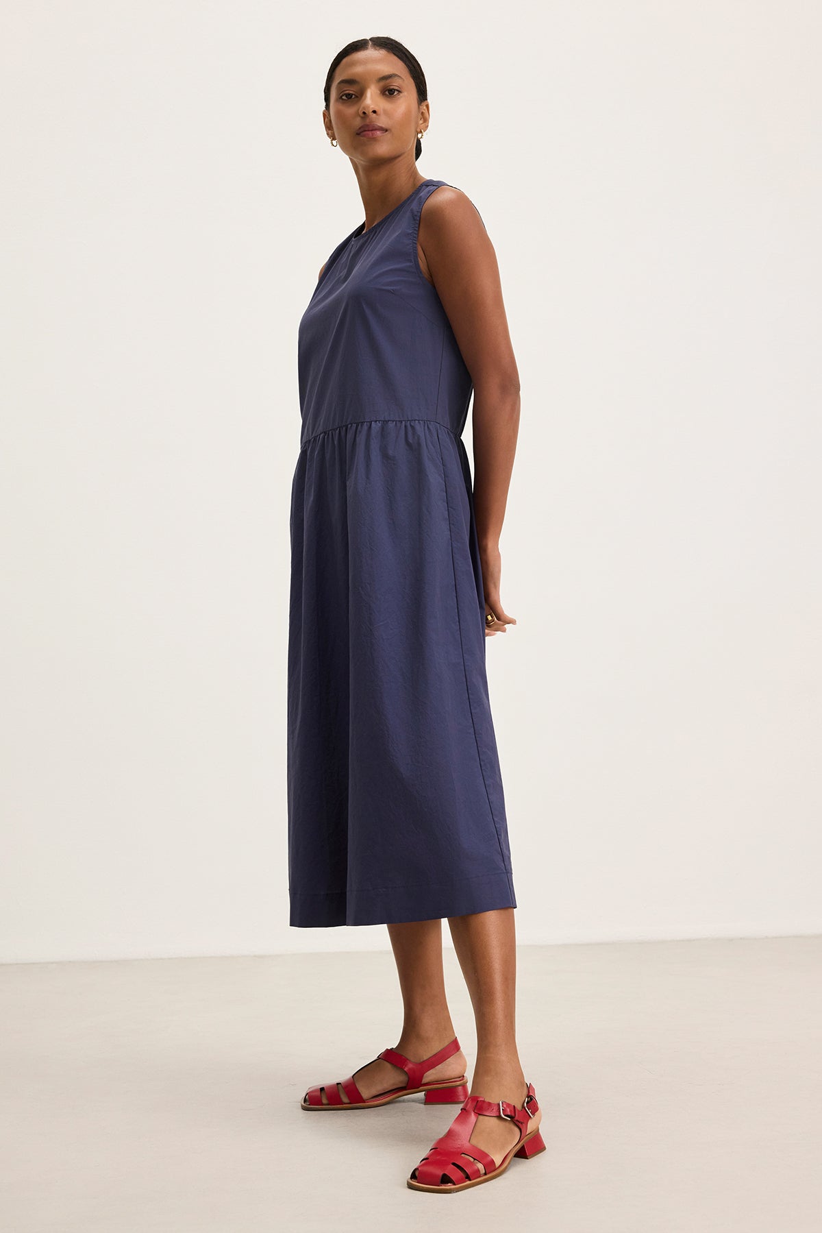 A person is wearing the MASHA DRESS, a sleeveless navy midi-length dress with an elastic waist from Velvet by Graham & Spencer, paired with red sandals, standing against a plain background.-38662692536513