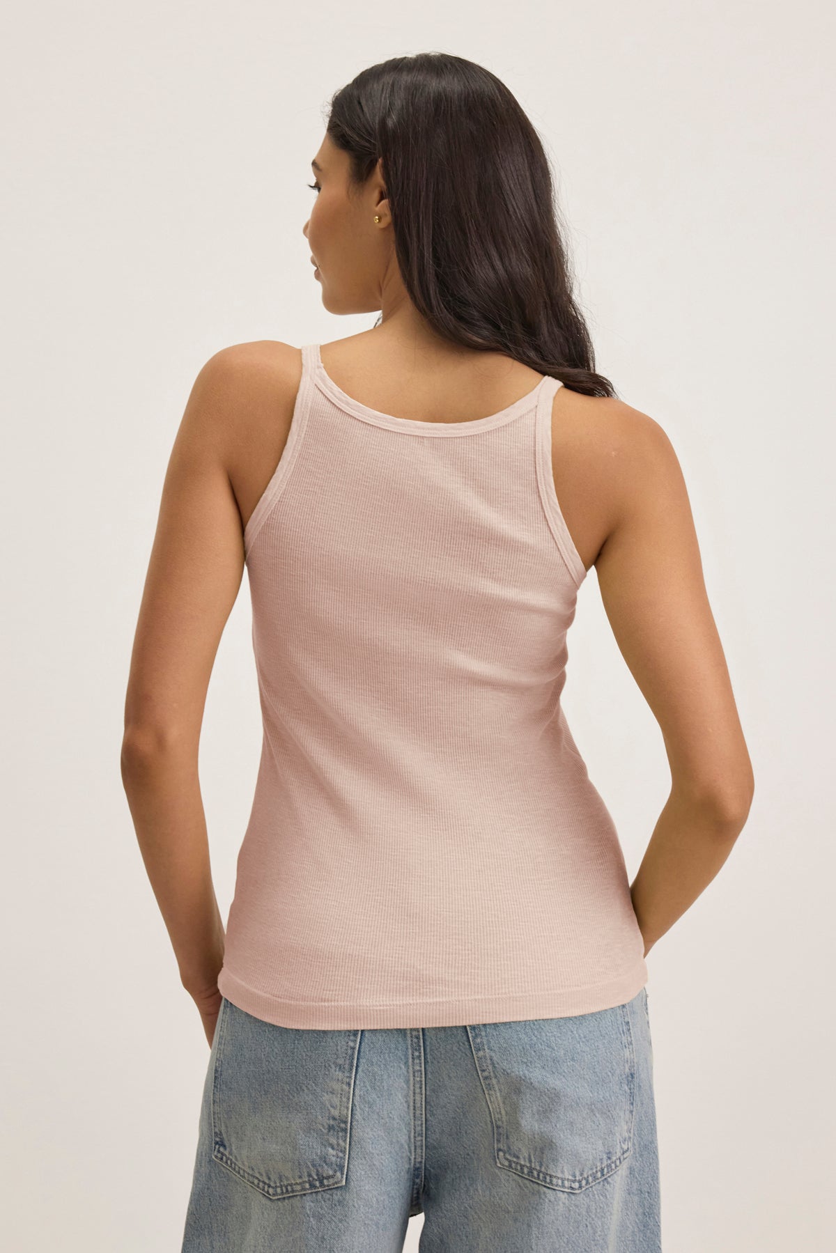 A person with long hair is seen from behind wearing a light pink ALIZA RIBBED COTTON LAYERING TANK from Velvet by Graham & Spencer and blue jeans.-38928214556865