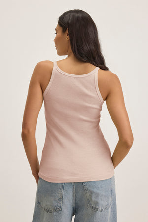 A person with long hair is seen from behind wearing a light pink ALIZA RIBBED COTTON LAYERING TANK from Velvet by Graham & Spencer and blue jeans.