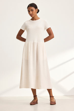 An individual is dressed in the ITZA DRESS by Velvet by Graham & Spencer, paired with brown sandals, standing against a light background.