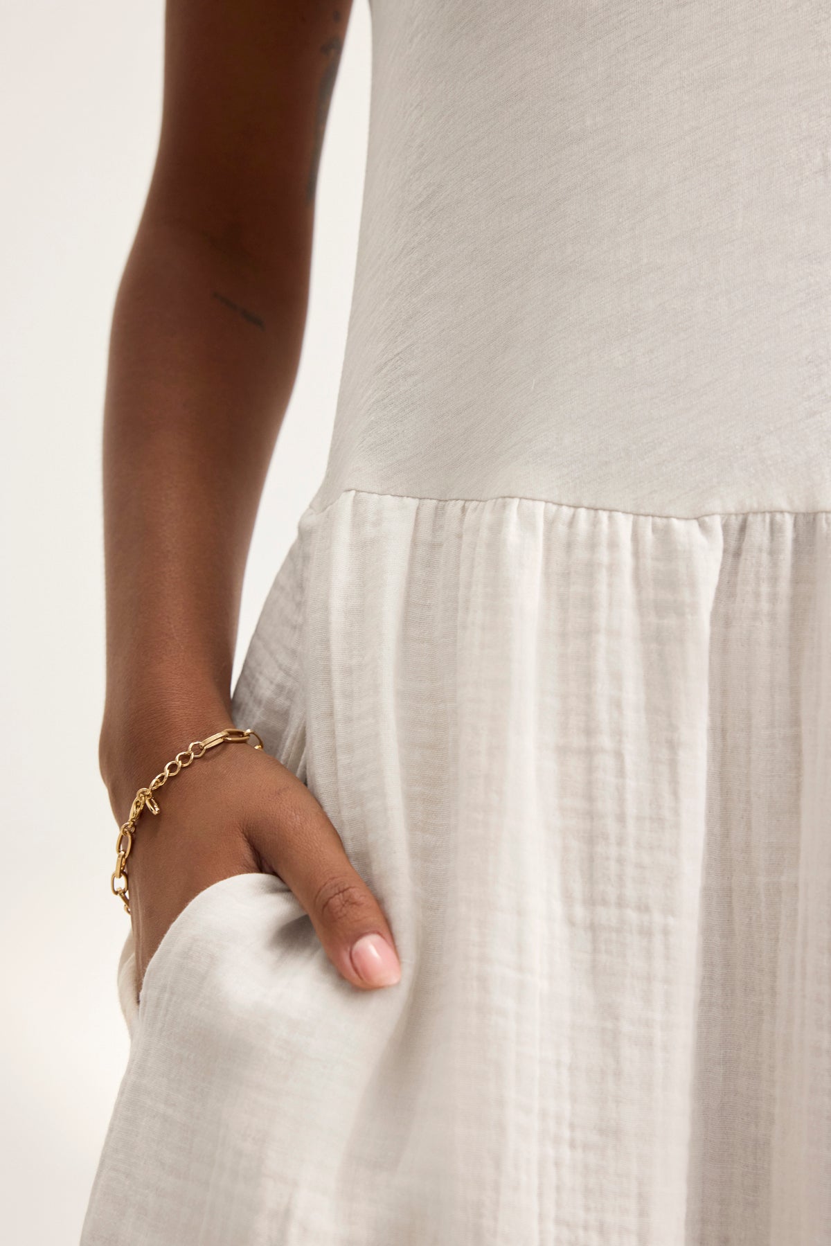 An individual wearing the ITZA DRESS by Velvet by Graham & Spencer rests their hand in a pocket of the white dress, and a gold bracelet adorns their wrist.-38918714491073