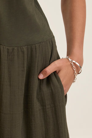 An individual wearing the ITZA DRESS by Velvet by Graham & Spencer, with their right hand in the pocket. Their wrist features a silver bracelet along with a chain bracelet.