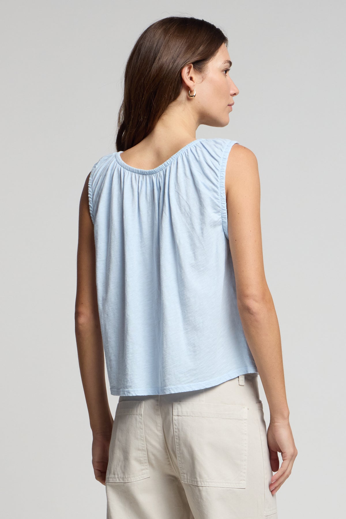 A woman faces away, wearing the JUNA TANK TOP by Velvet by Graham & Spencer in light blue with beige pants, set against a plain background.-41569247756481
