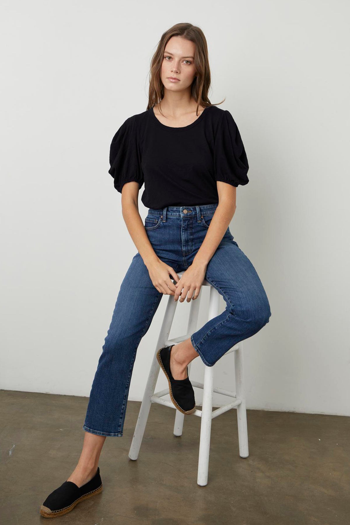   A woman is sitting on a stool wearing black jeans and a black Velvet by Graham & Spencer KIERA PUFF SLEEVE TEE. 