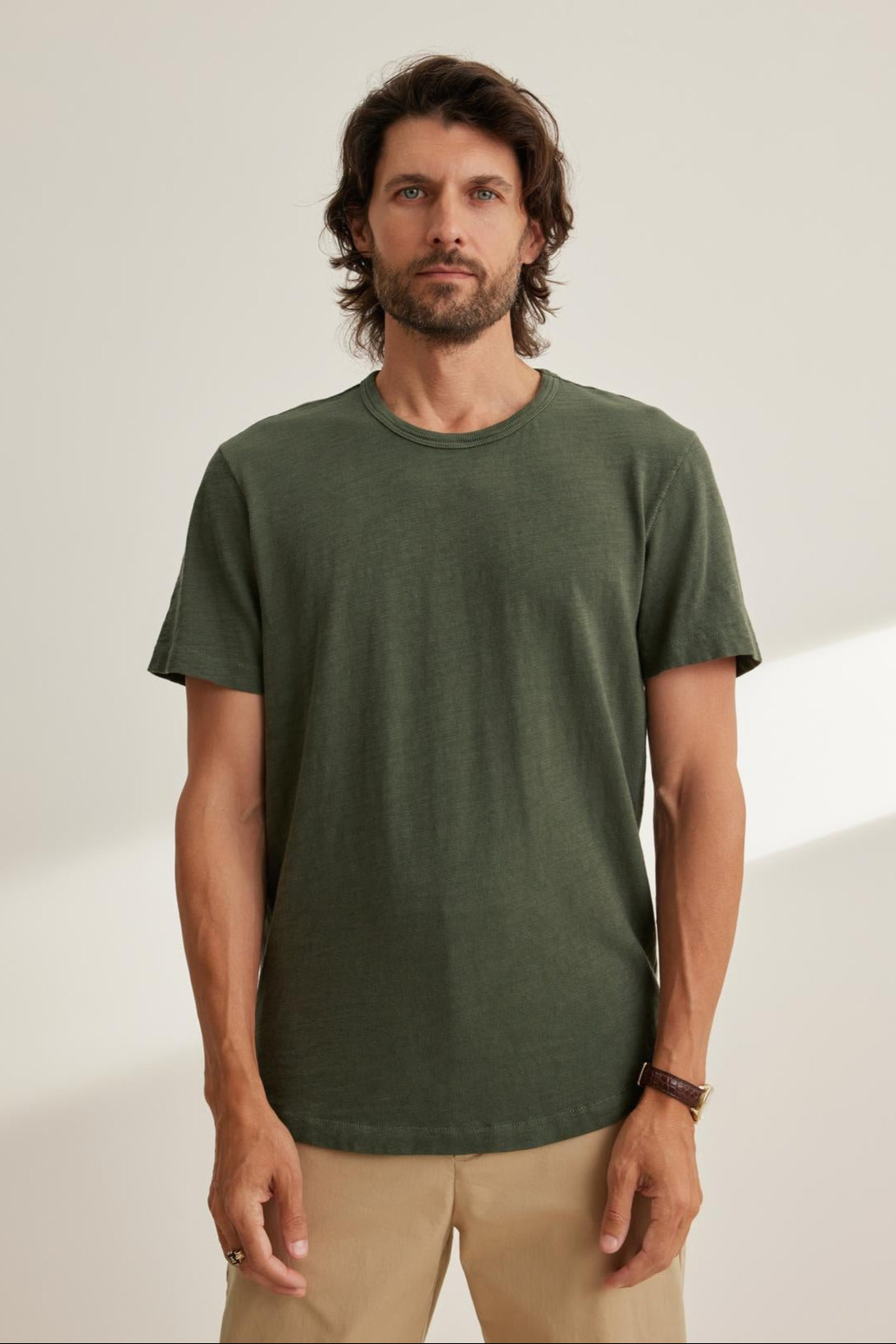 A man with medium-length hair and a beard is wearing the SPADER TEE, a relaxed fit green Peruvian cotton slub t-shirt by Velvet by Graham & Spencer, paired with beige pants. He stands against a plain background.-38643352731841