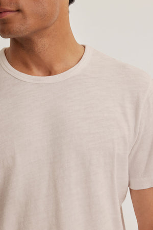 Someone wearing the SPADER TEE by Velvet by Graham & Spencer, featuring a plain light color, classic crew neckline, and relaxed fit, set against a neutral background with their face partially out of frame.