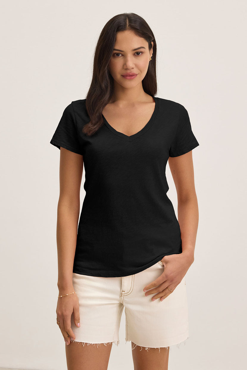 A person with long hair wearing Velvet by Graham & Spencer's LILITH TEE, made of luxurious cotton slub fabric, and beige shorts stands against a plain background, exuding a relaxed yet flattering fit.