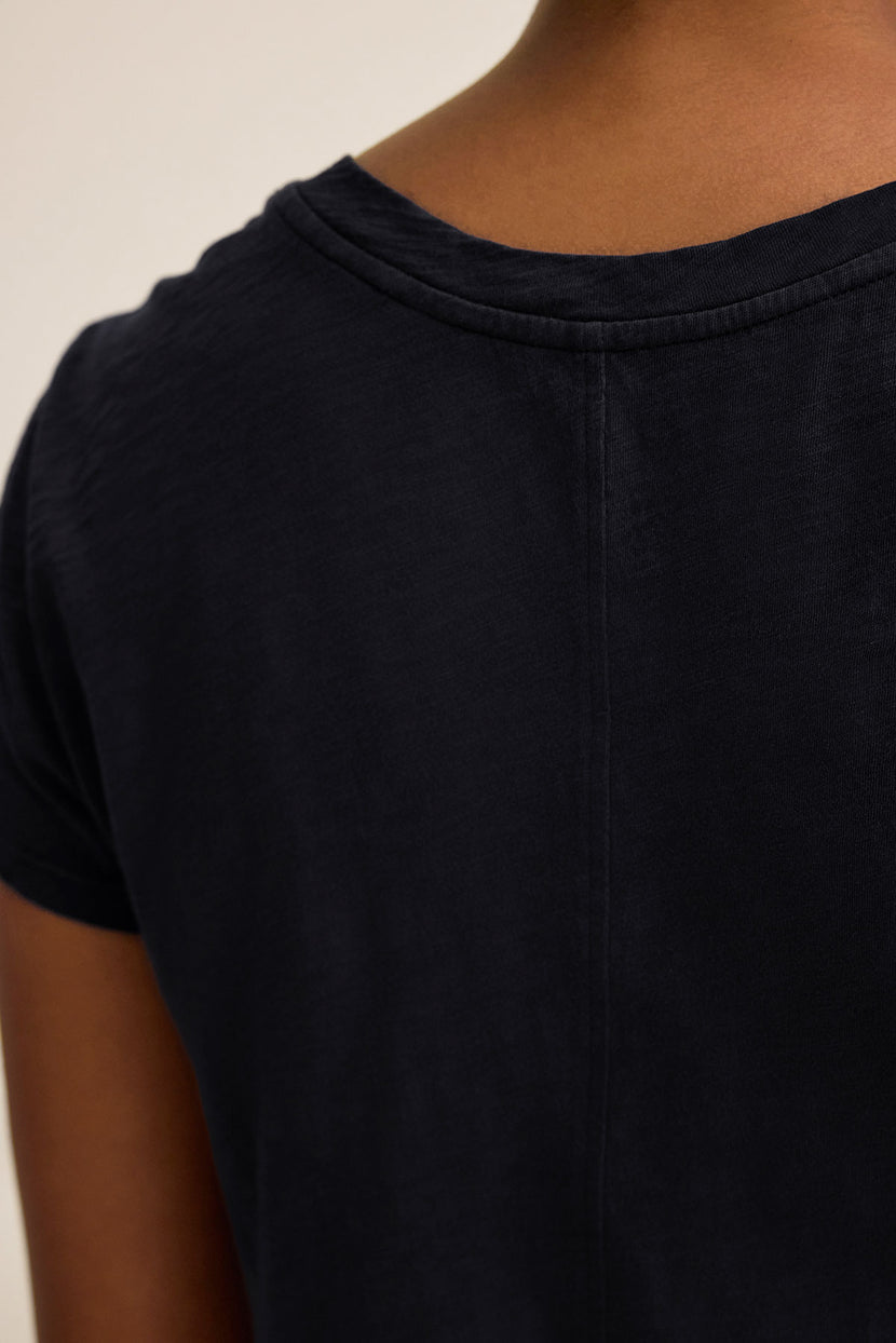 Close-up of the back of a person wearing the ODELIA TEE by Velvet by Graham & Spencer, a dark short-sleeve shirt made from premium cotton, showcasing its classic crew neckline and seam details.