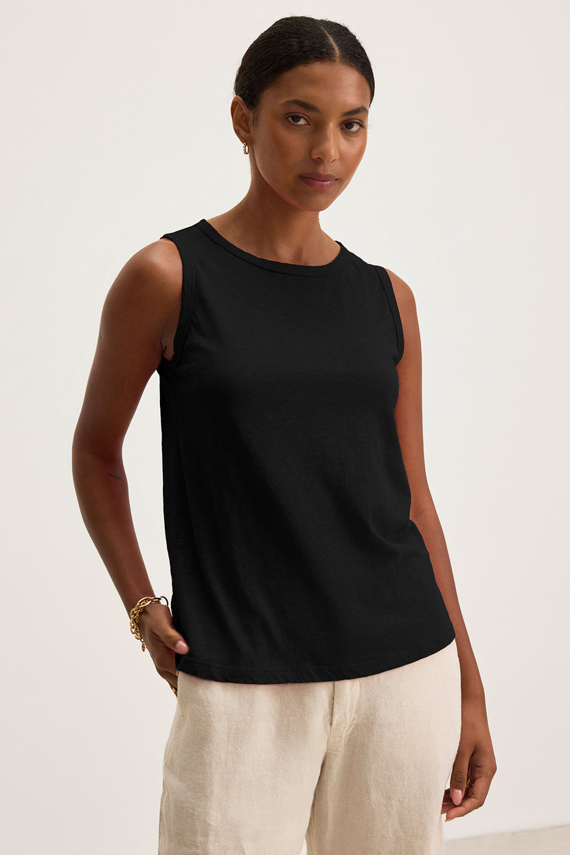 A person wearing the timeless Taurus Tank Top, a black sleeveless piece by Velvet by Graham & Spencer, and light-colored pants stands against a plain background.