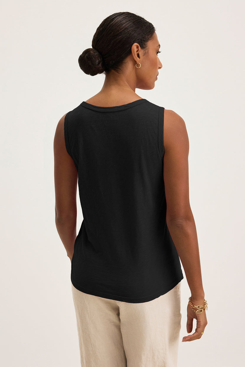 A person in a TAURUS TANK TOP by Velvet by Graham & Spencer, a timeless crew neck black sleeveless design, pairs it with beige pants, facing away with hair styled in a bun.