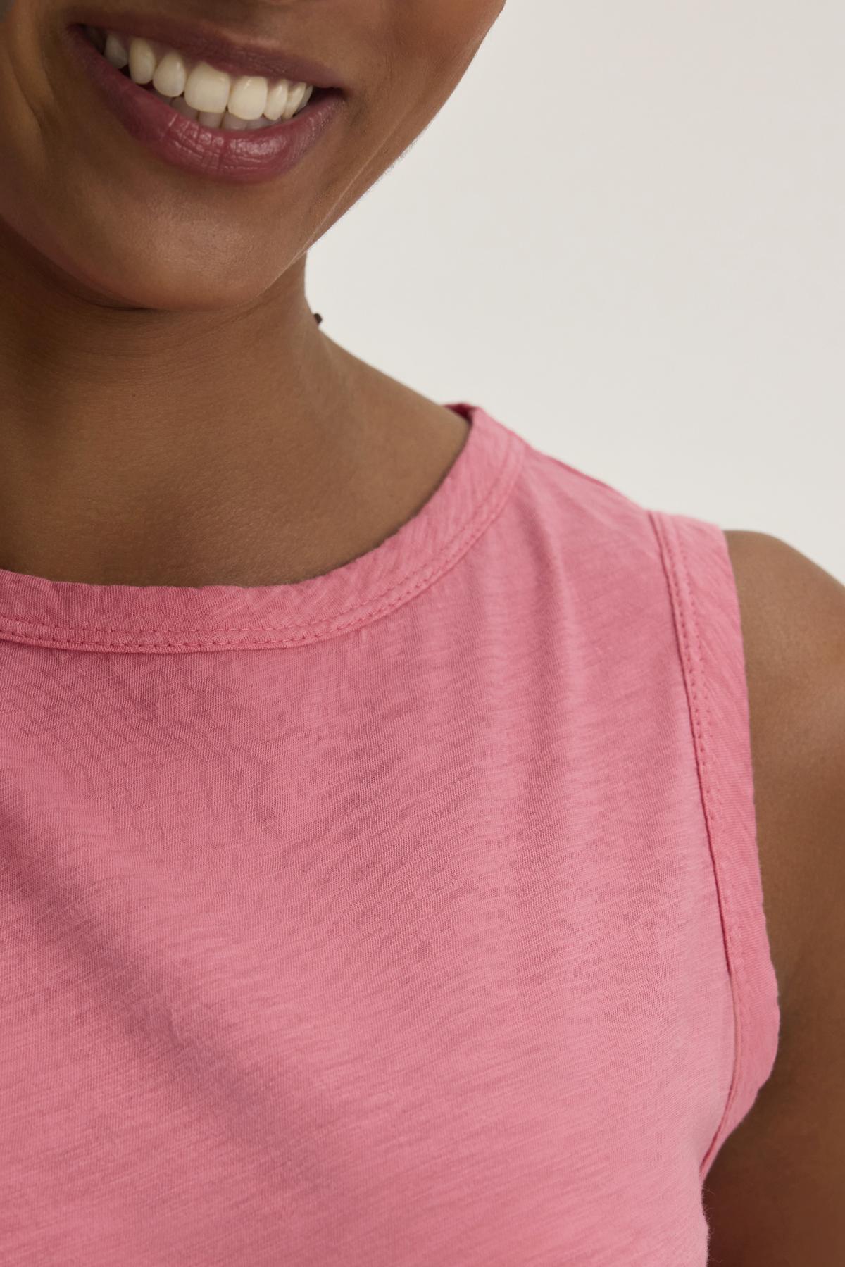   A person smiles, wearing the TAURUS TANK TOP by Velvet by Graham & Spencer—an essential sleeveless pink top made from textured cotton slub. 