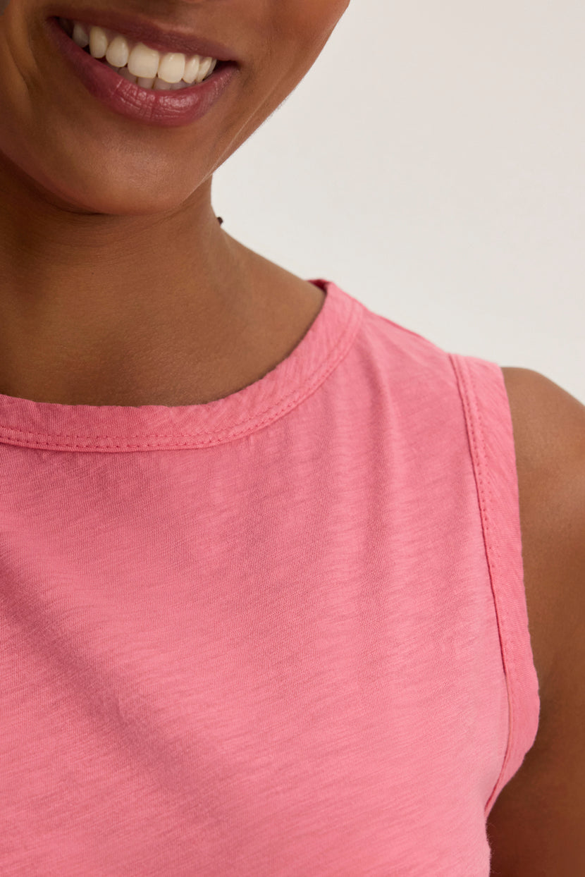 A smiling person wears the TAURUS TANK TOP by Velvet by Graham & Spencer, a pink sleeveless essential adding timeless elegance to any wardrobe.