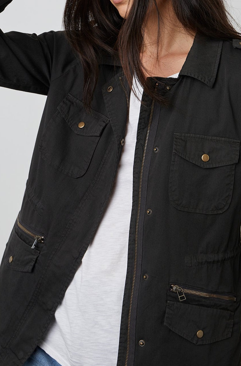   A woman wearing a black Velvet by Graham & Spencer RUBY LIGHT-WEIGHT ARMY JACKET with zippers and pockets. 