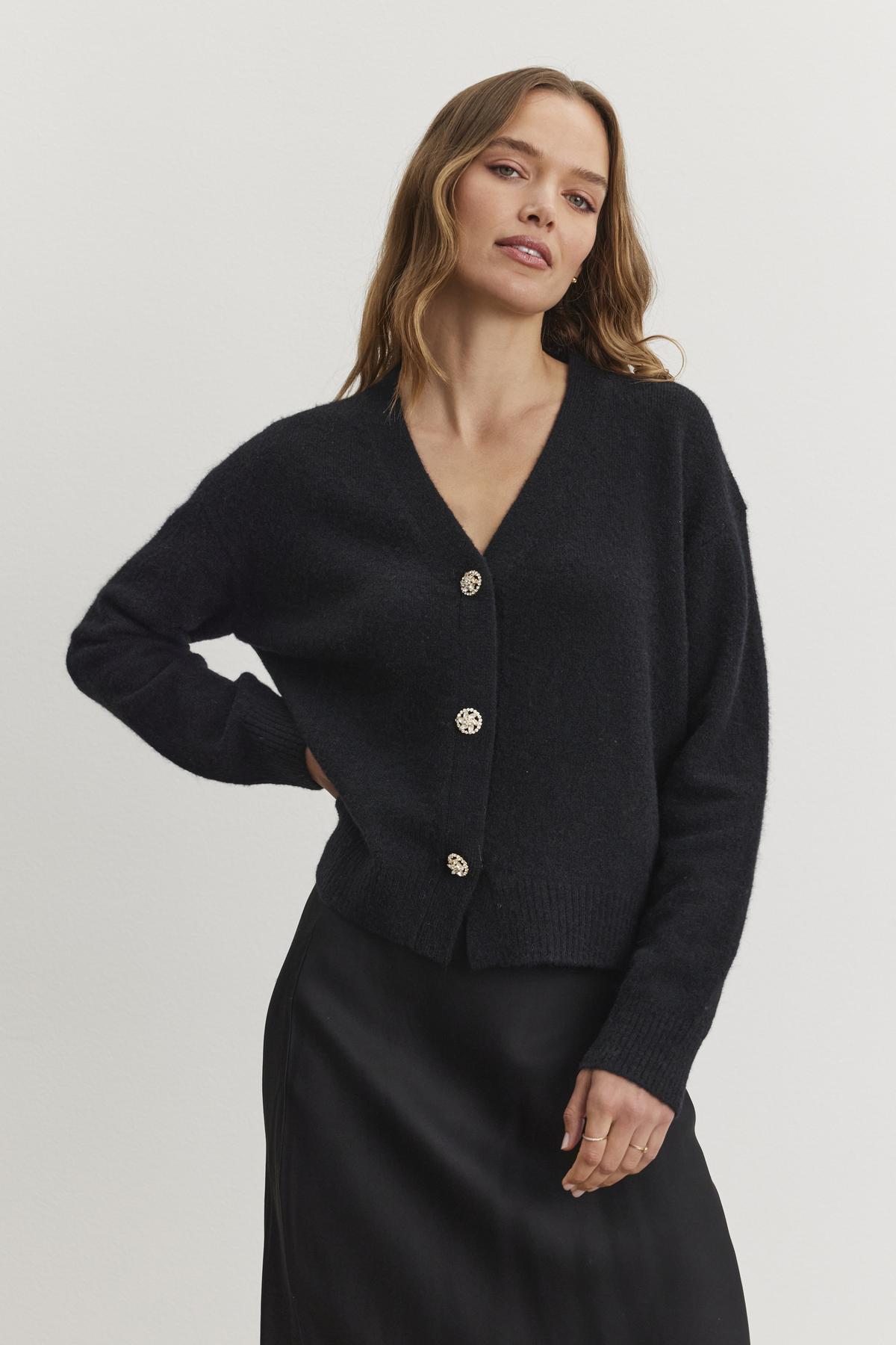   A person wearing the MARTI ALPACA EMBELLISHED CARDIGAN by Velvet by Graham & Spencer, paired with a black skirt, stands against a plain background. 