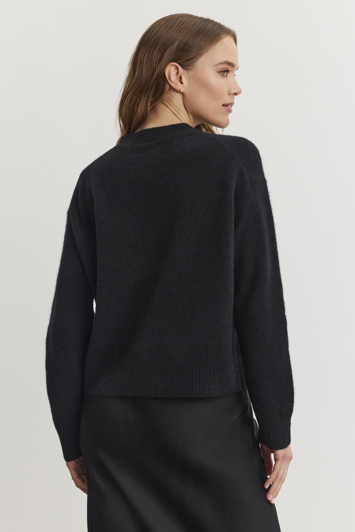   A woman is wearing the MARTI ALPACA EMBELLISHED CARDIGAN by Velvet by Graham & Spencer, paired with a black skirt, and is facing slightly to the side against a plain white background. 