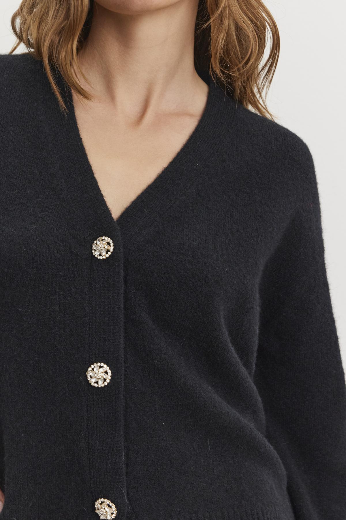   Individual dressed in the MARTI ALPACA EMBELLISHED CARDIGAN by Velvet by Graham & Spencer, featuring a dark V-neck with four decorative buttons. 