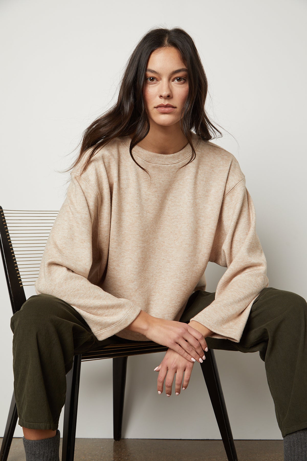   The model is sitting on a chair in a Velvet by Graham & Spencer NIA DOUBLE KNIT CROPPED CREW, exuding both comfort and style. 