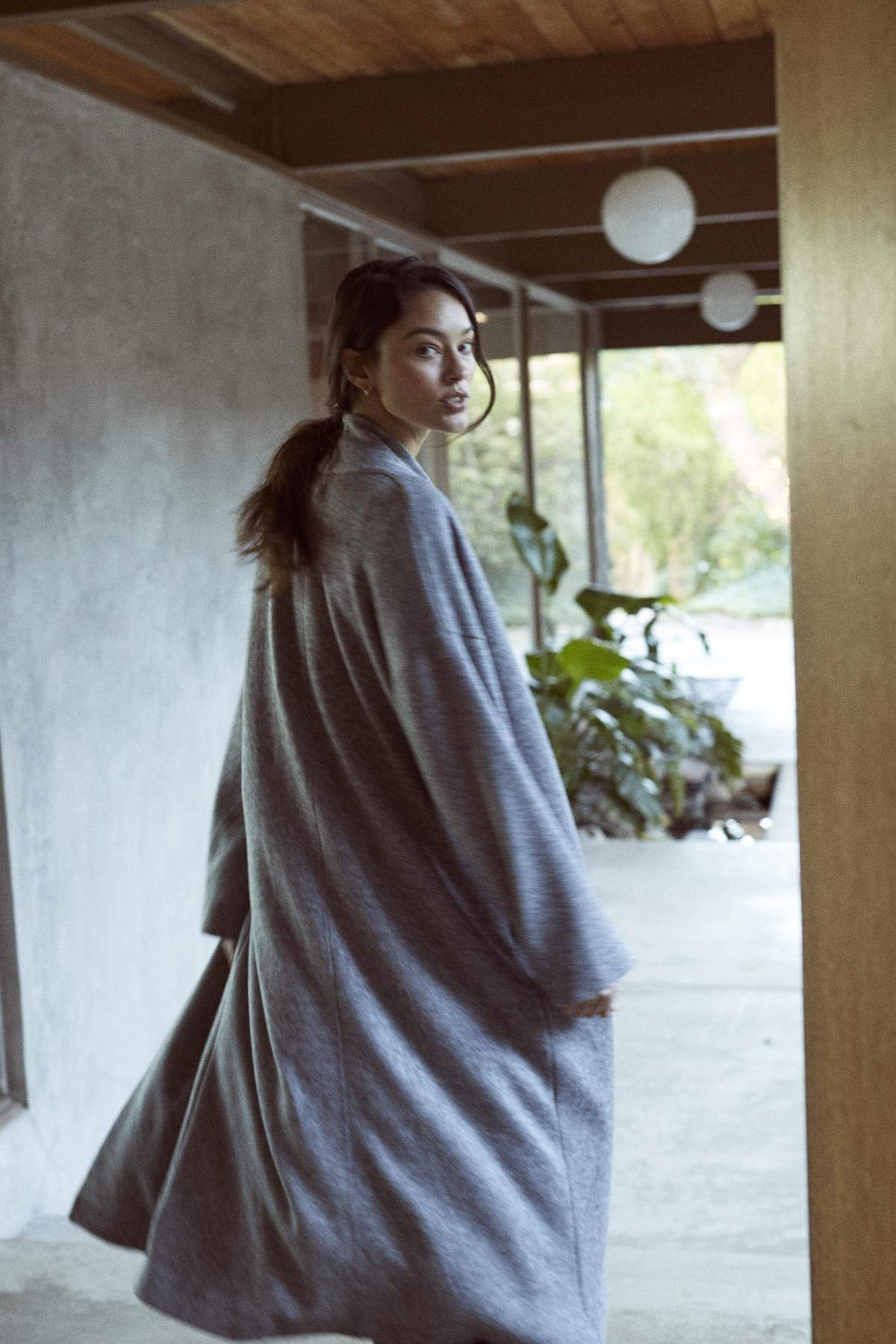   A woman in a cozy grey Velvet by Graham & Spencer Patricia Double Knit Duster Cardigan walking down a hallway. 