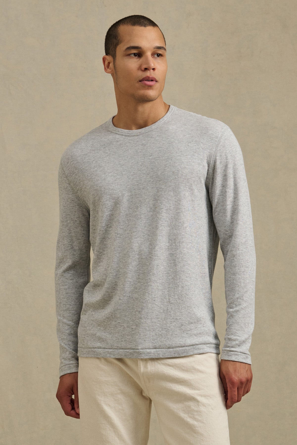 A person wears the Velvet by Graham & Spencer COLTON CREW in light gray with off-white pants, standing against a plain beige background.-41008943136961