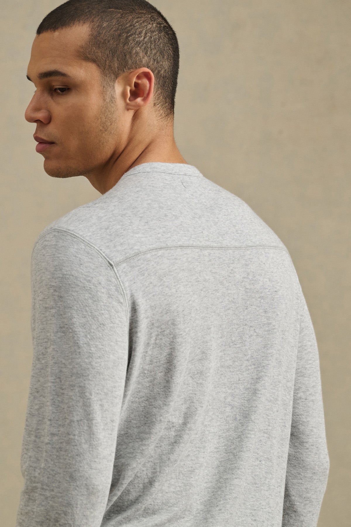 A man with short hair wears the Velvet by Graham & Spencer COLTON CREW, a light gray long-sleeve classic crewneck, facing slightly away from the camera against a neutral background.-41008943038657