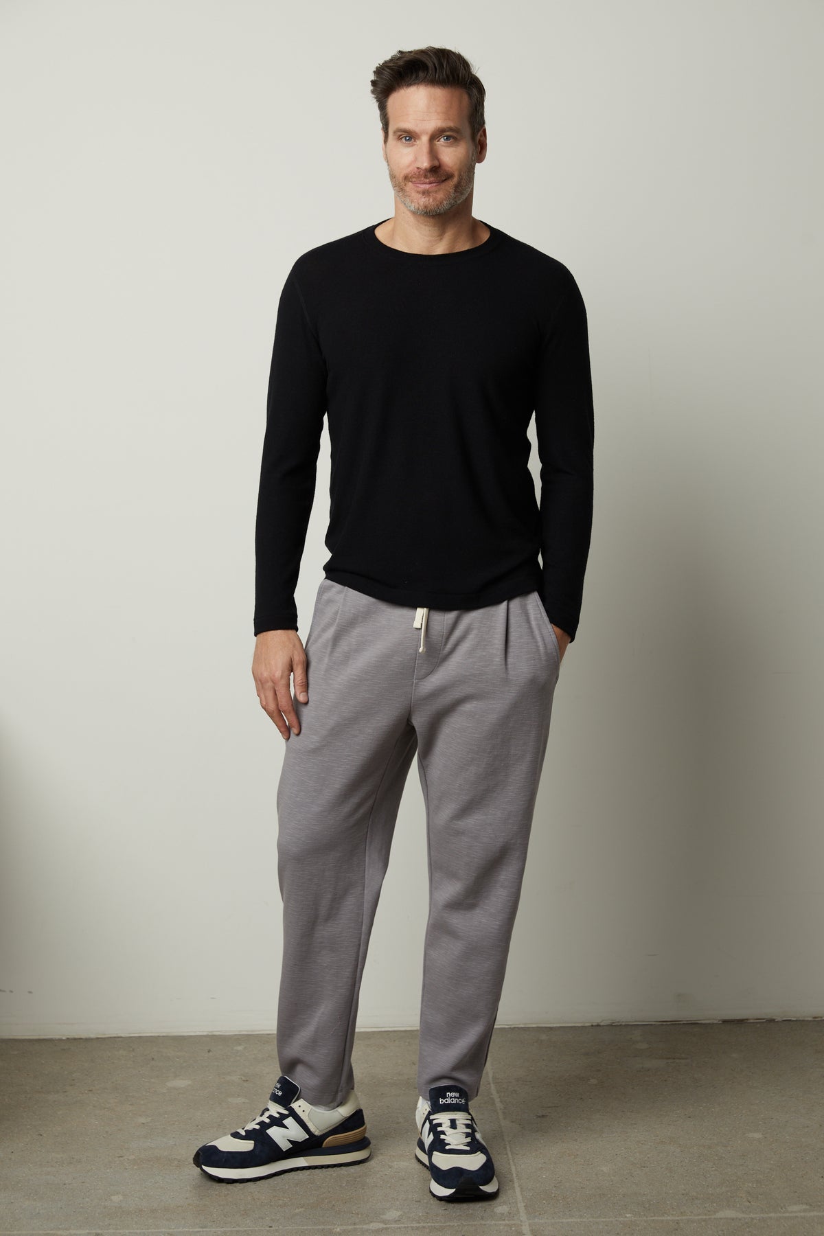   A man wearing a Velvet by Graham & Spencer modern comfort black sweater and signature cozy grey sweatpants. 
