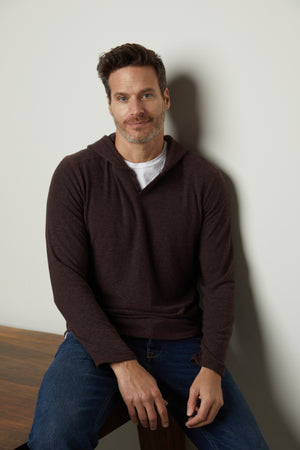 A man sitting on a table wearing jeans and a Velvet by Graham & Spencer BYRD COZY JERSEY HOODIE.