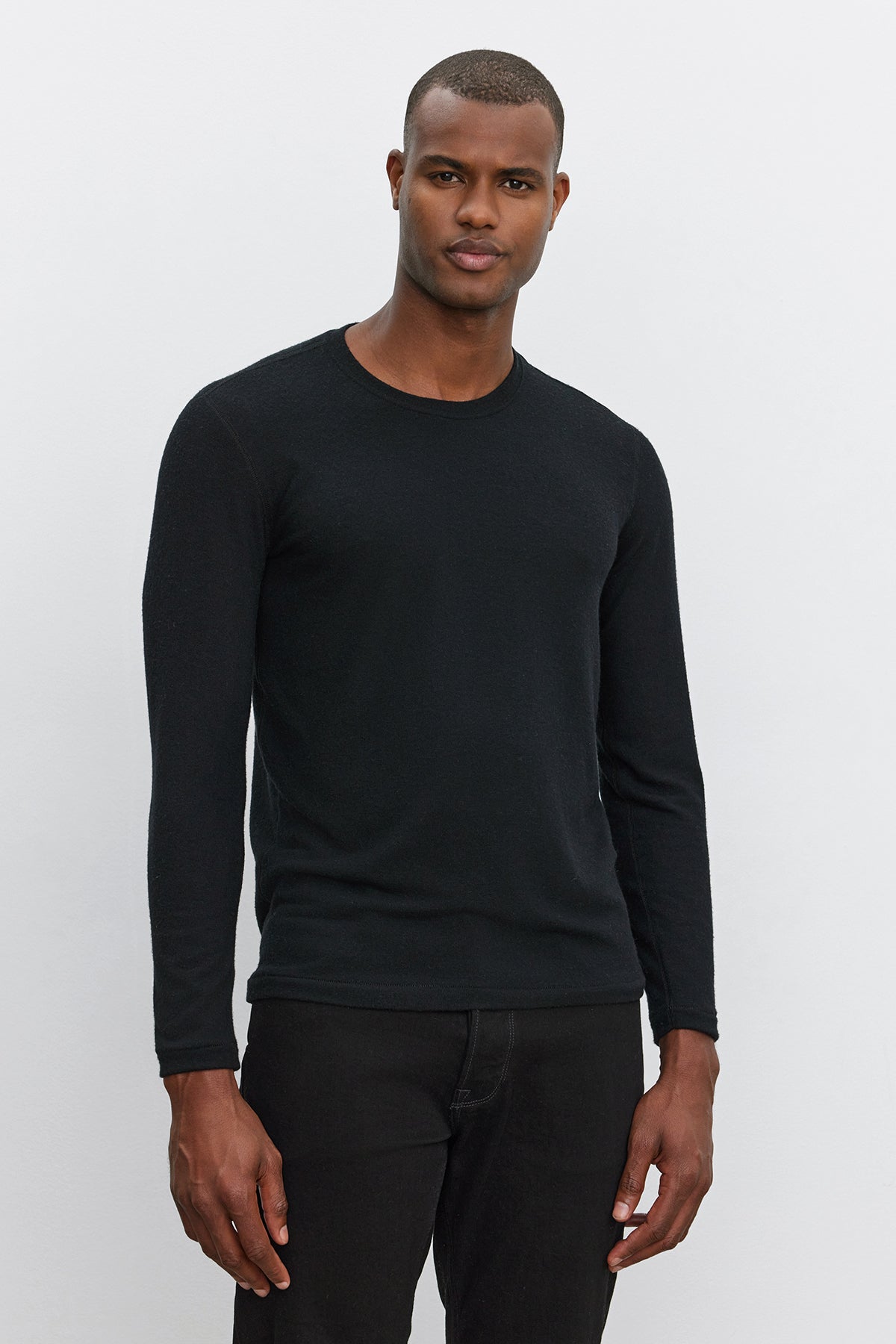 A man wearing a Velvet by Graham & Spencer BECKER CREW black fitted crew neck long-sleeve shirt and black pants stands against a plain white background, looking at the camera. The ultra-soft jersey fabric makes it perfect for daily wear.-37893852856513