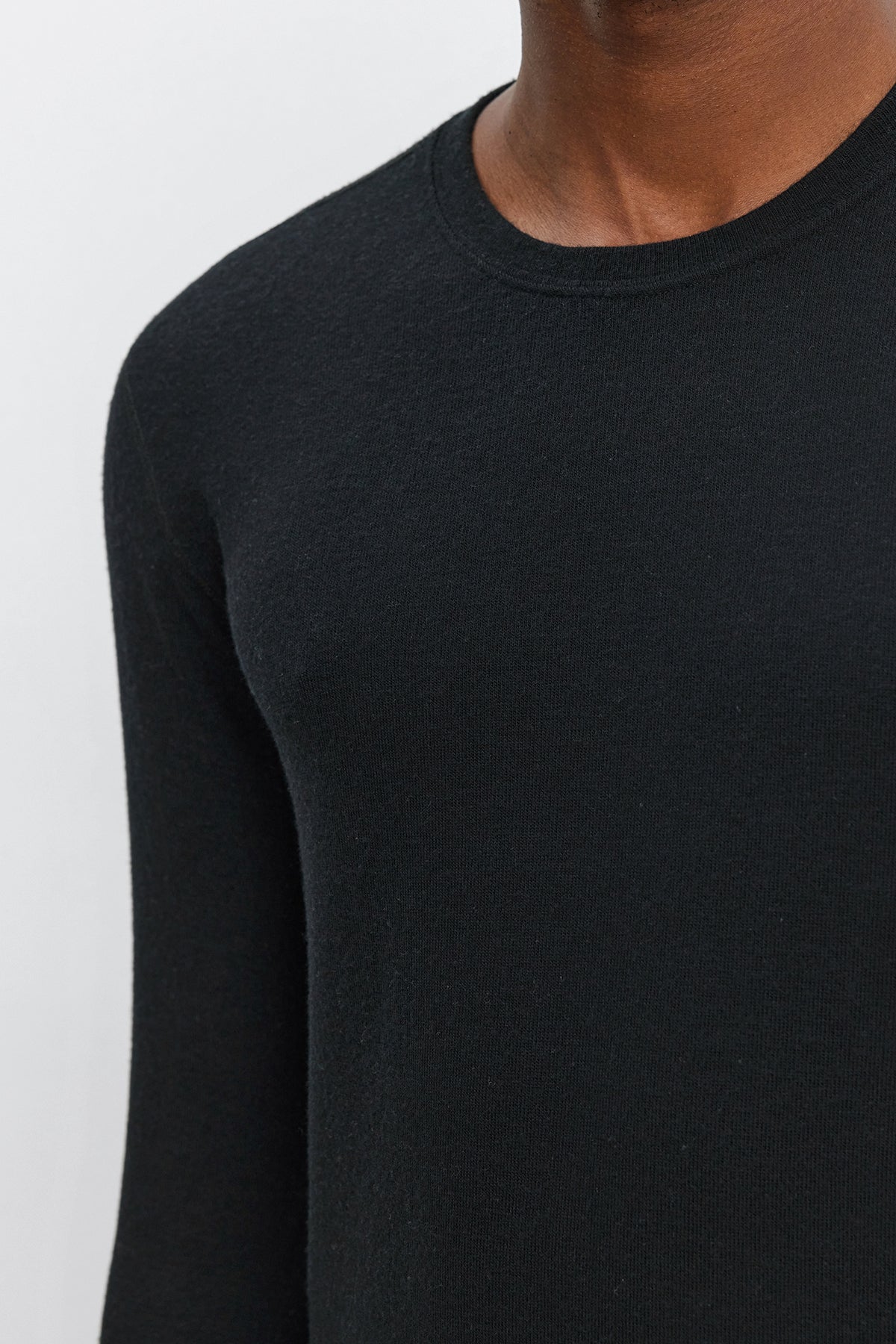   Close-up of a person wearing the BECKER CREW, an ultra-soft black jersey long-sleeve shirt from Velvet by Graham & Spencer. The photo showcases the upper torso and partial neck of the individual, set against a plain background. 