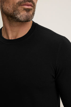 A man with a short beard wears the Velvet by Graham & Spencer BECKER CREW, a fitted black long-sleeve crew neck shirt, photographed from the shoulders up against a plain background.