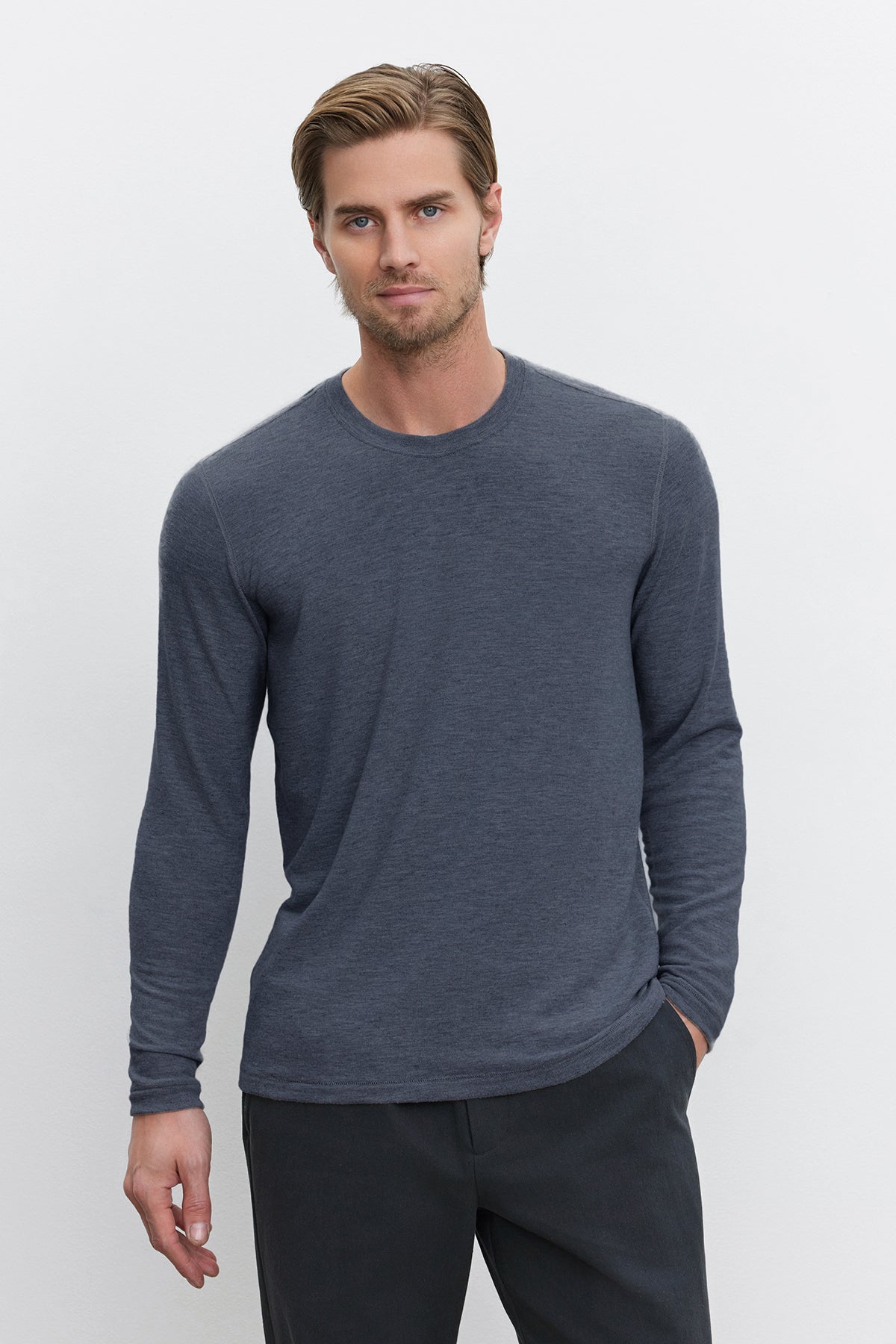 Dressed in the BECKER CREW by Velvet by Graham & Spencer, a man strikes a stylish pose against a plain white background, effortlessly showcasing everyday fashion in his cozy jersey gray long-sleeve shirt and dark pants.-38282364223681