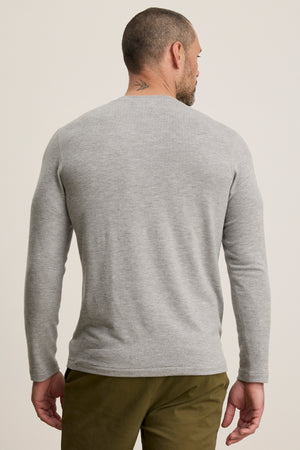A man faces away from the camera, wearing the BECKER CREW by Velvet by Graham & Spencer—a fitted light gray crew neck long-sleeve shirt paired with olive green pants, perfect for effortless daily wear.