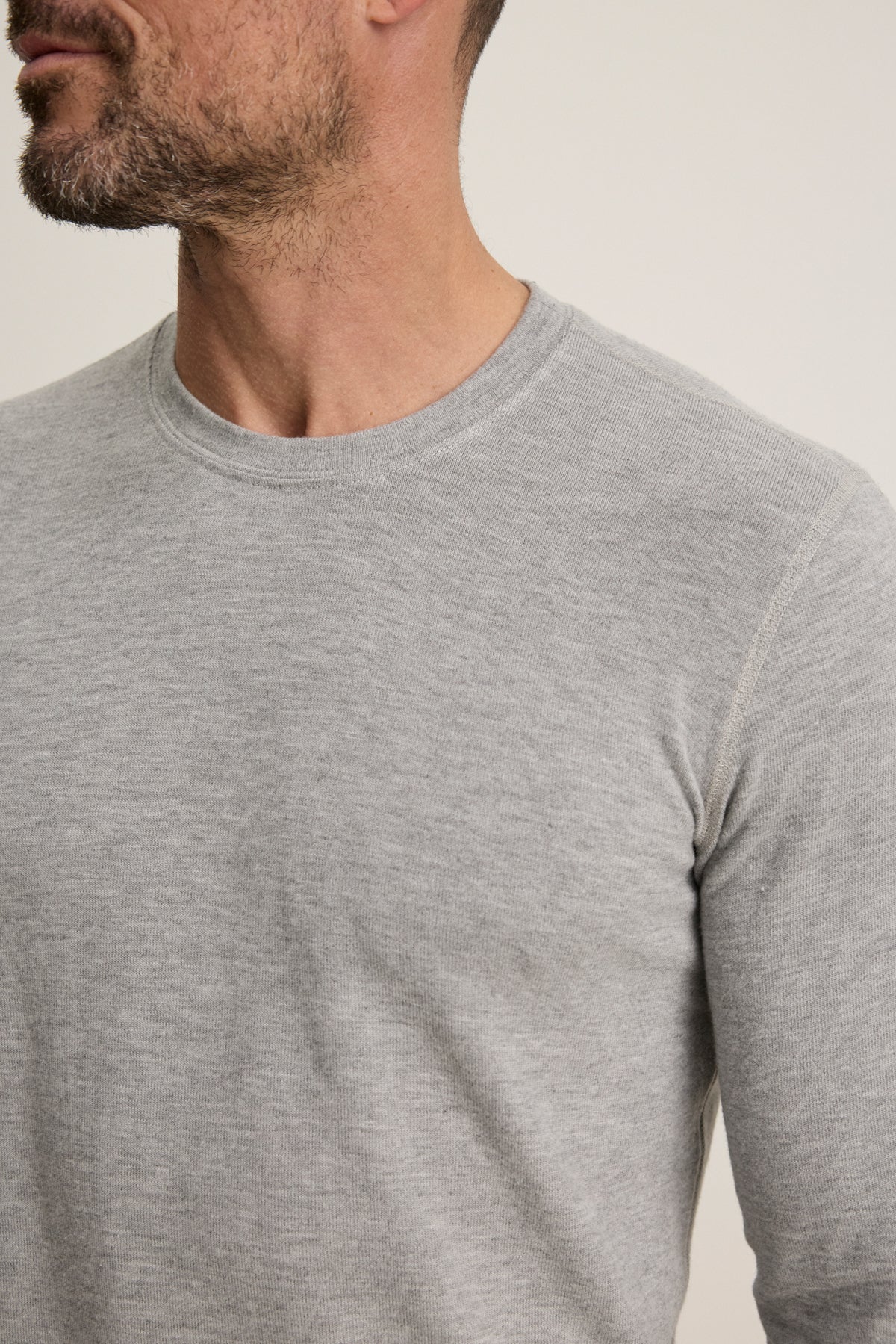 A man with short facial hair is shown from the shoulders up, wearing the BECKER CREW by Velvet by Graham & Spencer—a light grey, fitted crew neck sweater made from cozy jersey, ideal for everyday wear.-39680468746433