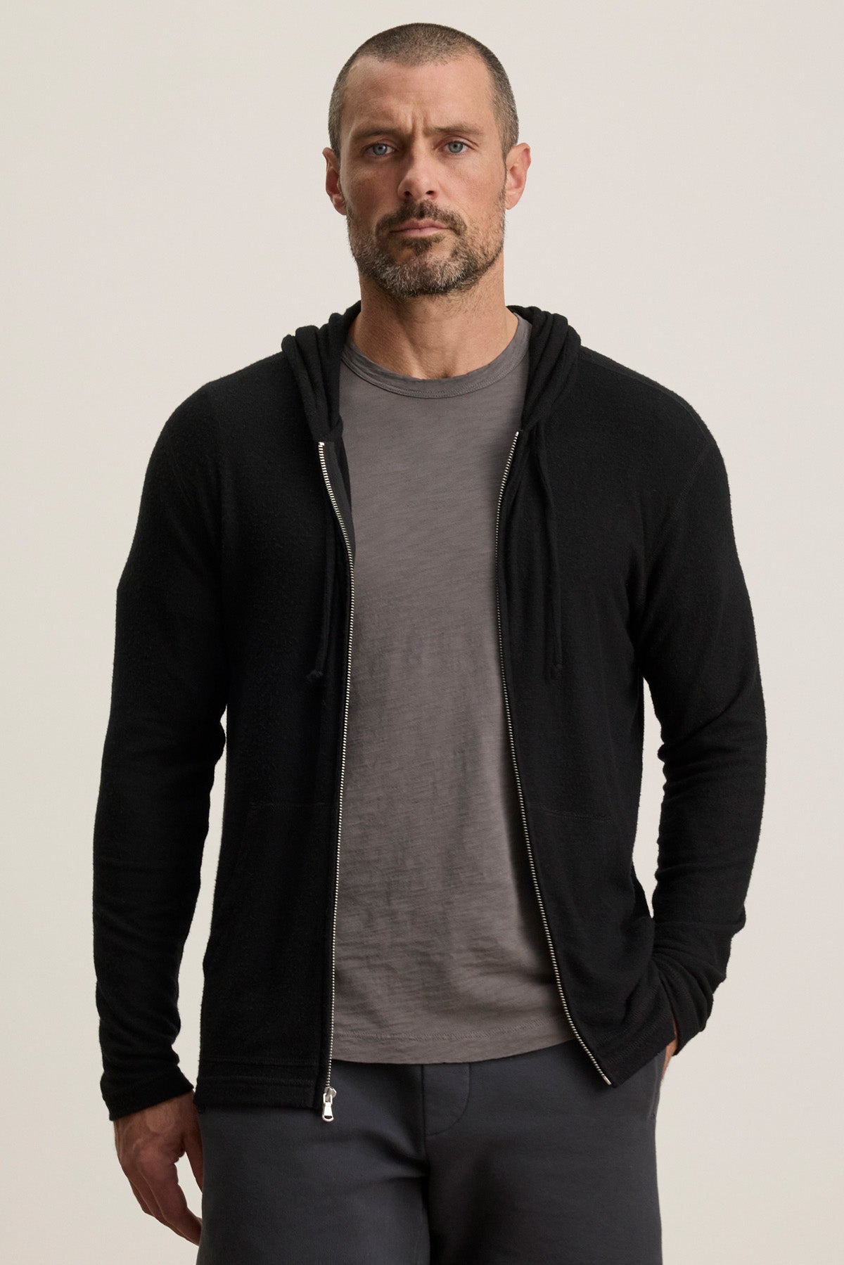 A man with a shaved head and beard wears a gray LOUDON HOODIE by Velvet by Graham & Spencer over a t-shirt, standing against a plain light background.