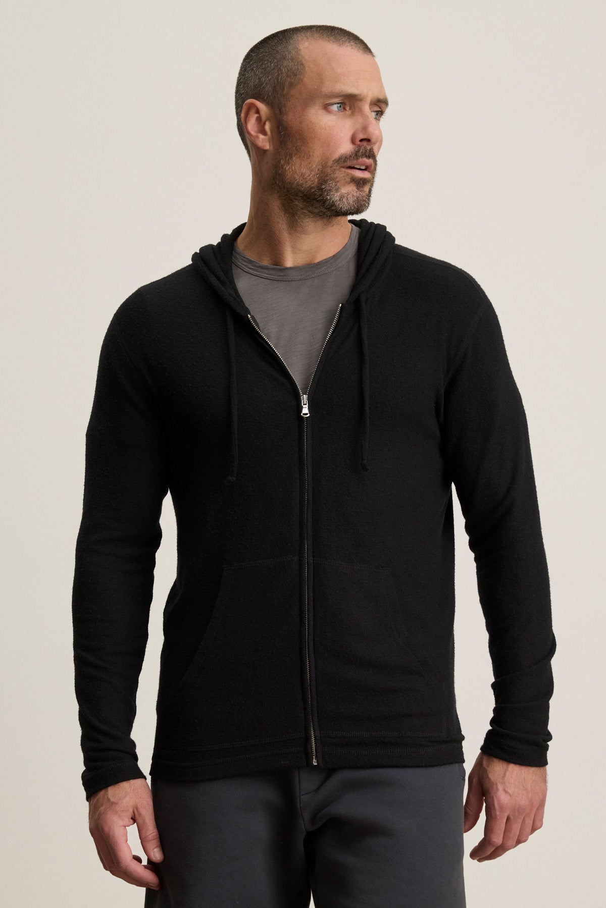 A man wears the LOUDON HOODIE by Velvet by Graham & Spencer in black, layered over a gray t-shirt, standing slightly turned against a plain light background.