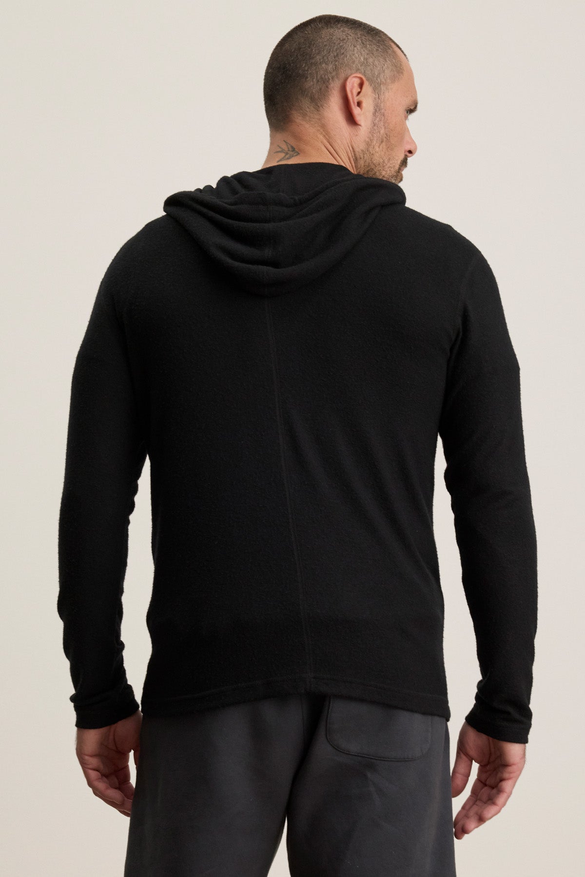 A man stands facing away, wearing the Velvet by Graham & Spencer LOUDON HOODIE in black with dark pants, set against a plain light background.-40452490952897