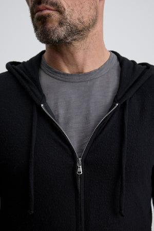 A man with a short beard wears a grey tee and the LOUDON HOODIE by Velvet by Graham & Spencer—a relaxed fit, black full-zip hoodie with drawstrings, partially unzipped. The cozy jersey image is cropped at his nose and chest.
