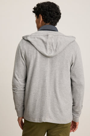 A person stands facing away in a relaxed fit LOUDON HOODIE by Velvet by Graham & Spencer, a light gray triblend cozy jersey full-zip, paired with olive green pants against a plain background.