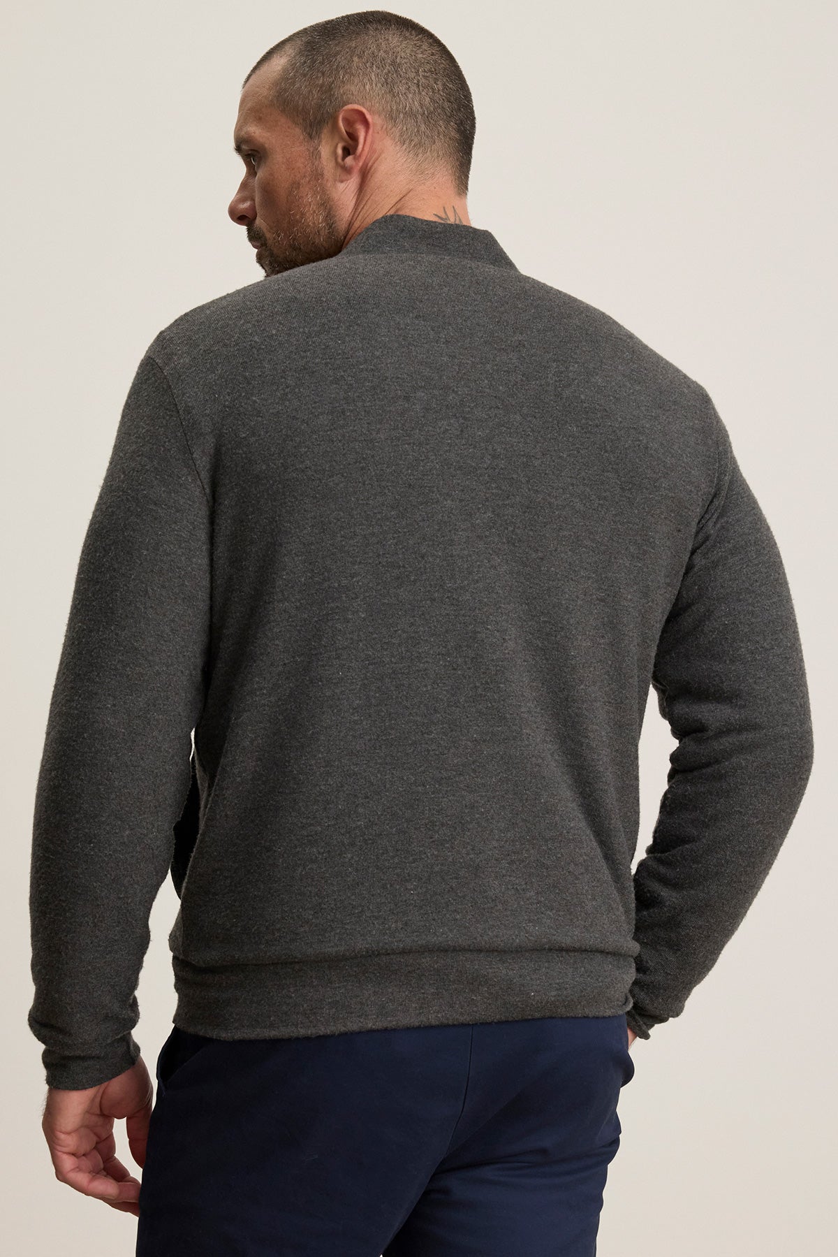 A man stands facing away, wearing the MILES JACKET by Velvet by Graham & Spencer—a dark gray casual jacket with a soft knit shell—paired with navy blue pants against a plain light background.-40247445815489