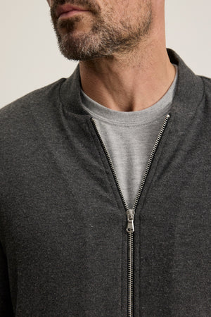 Close-up of a man wearing the MILES JACKET by Velvet by Graham & Spencer—a casual jacket with a soft knit shell—over a light gray t-shirt, showing only his lower face and upper torso.