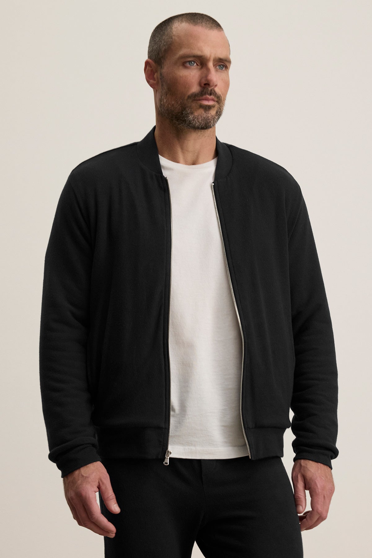 A man wearing a white t-shirt and the MILES JACKET by Velvet by Graham & Spencer stands facing forward against a plain, light-colored background.