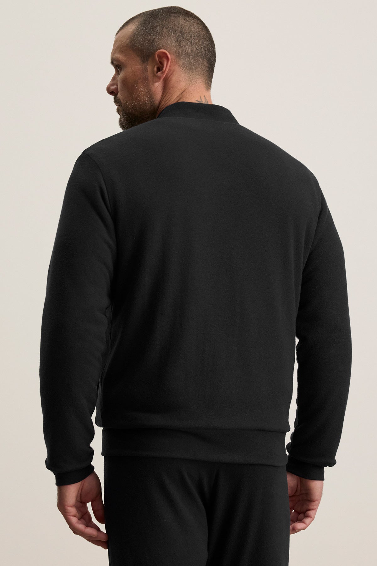 A man with short hair and a beard stands with his back to the camera, wearing the MILES JACKET by Velvet by Graham & Spencer and matching black pants against a plain background.-40307484131521
