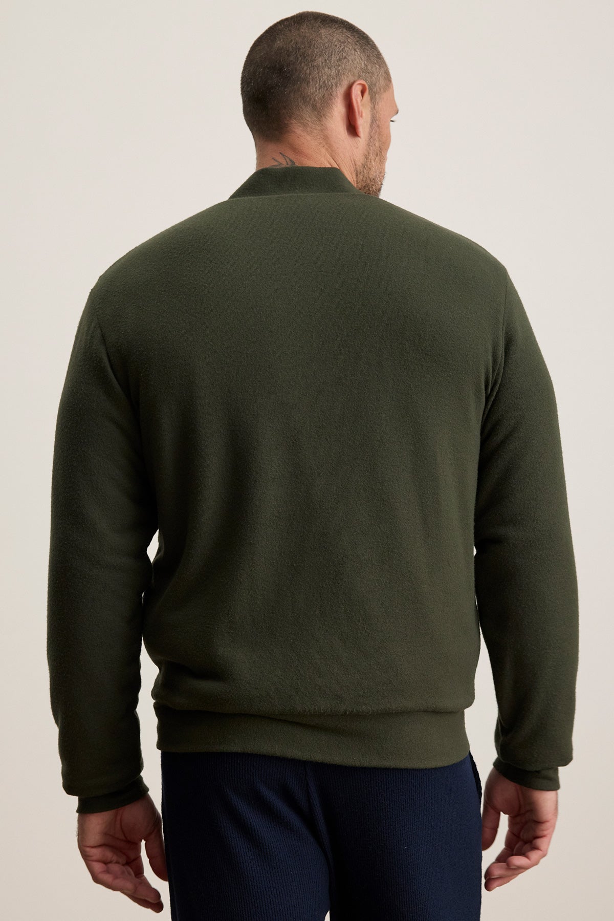 A man wearing the Velvet by Graham & Spencer MILES JACKET in dark green with navy pants stands facing away from the camera against a plain light background.