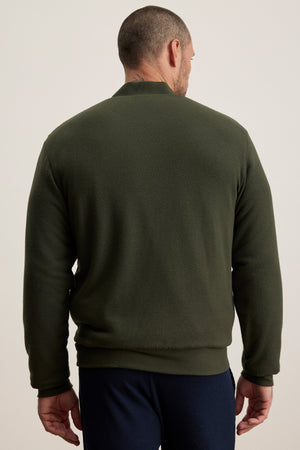 A man wearing the Velvet by Graham & Spencer MILES JACKET in dark green with navy pants stands facing away from the camera against a plain light background.