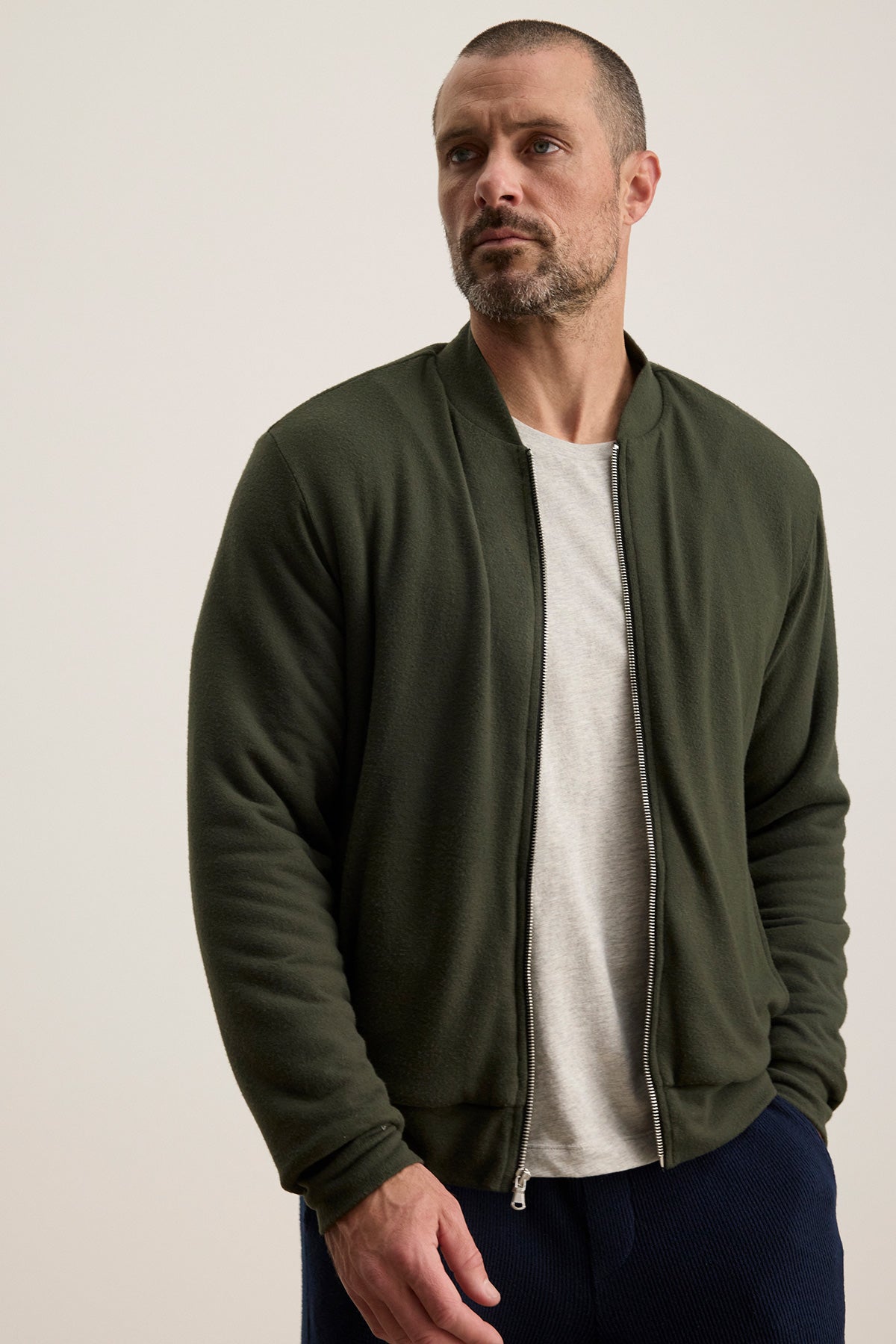 A man wearing the Velvet by Graham & Spencer MILES JACKET in olive over a light gray tee and dark pants stands against a plain light background.