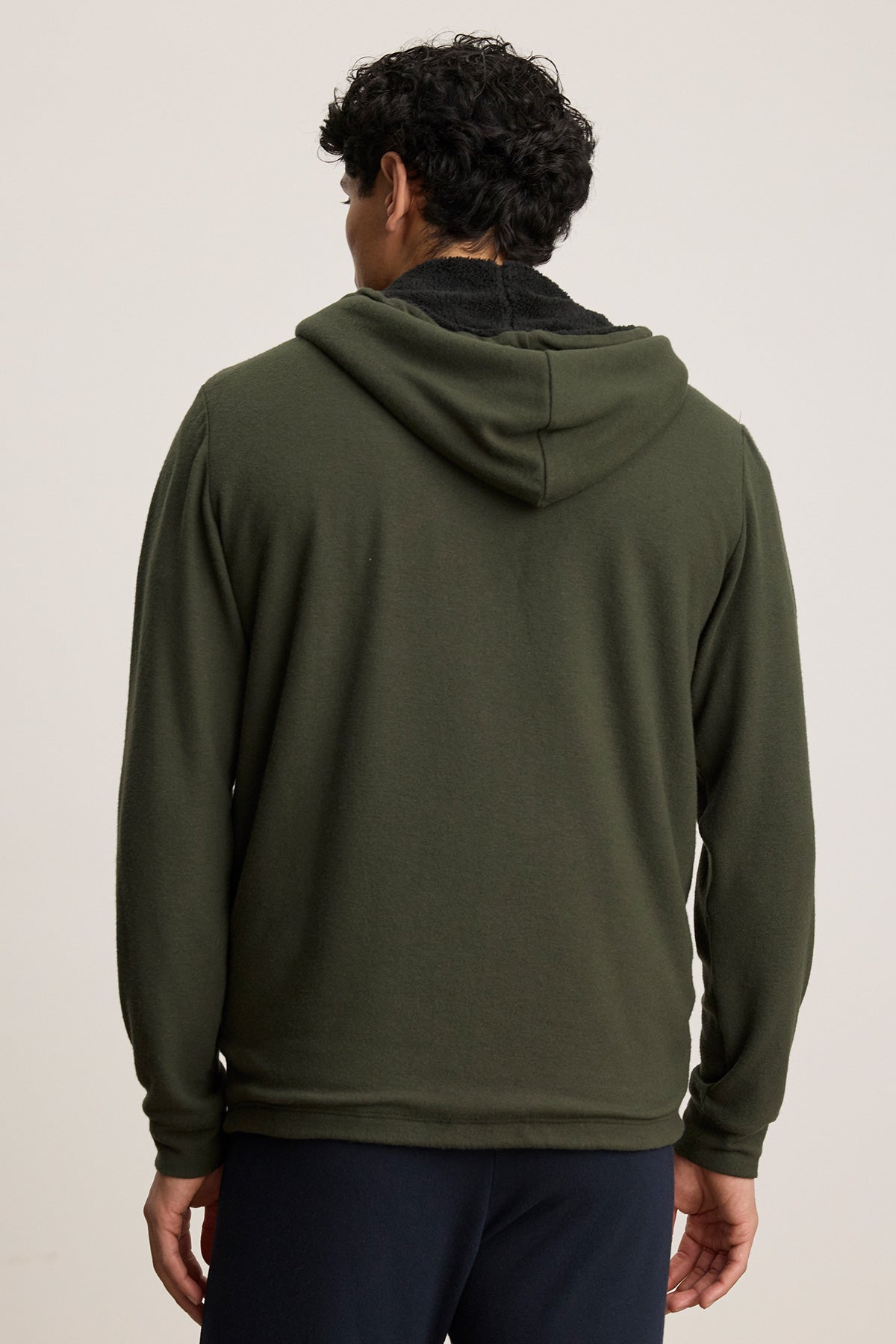 A person with short curly hair is seen from behind wearing the Velvet by Graham & Spencer SALVADORE HOODIE in olive green and dark pants against a plain background.-40277251358913