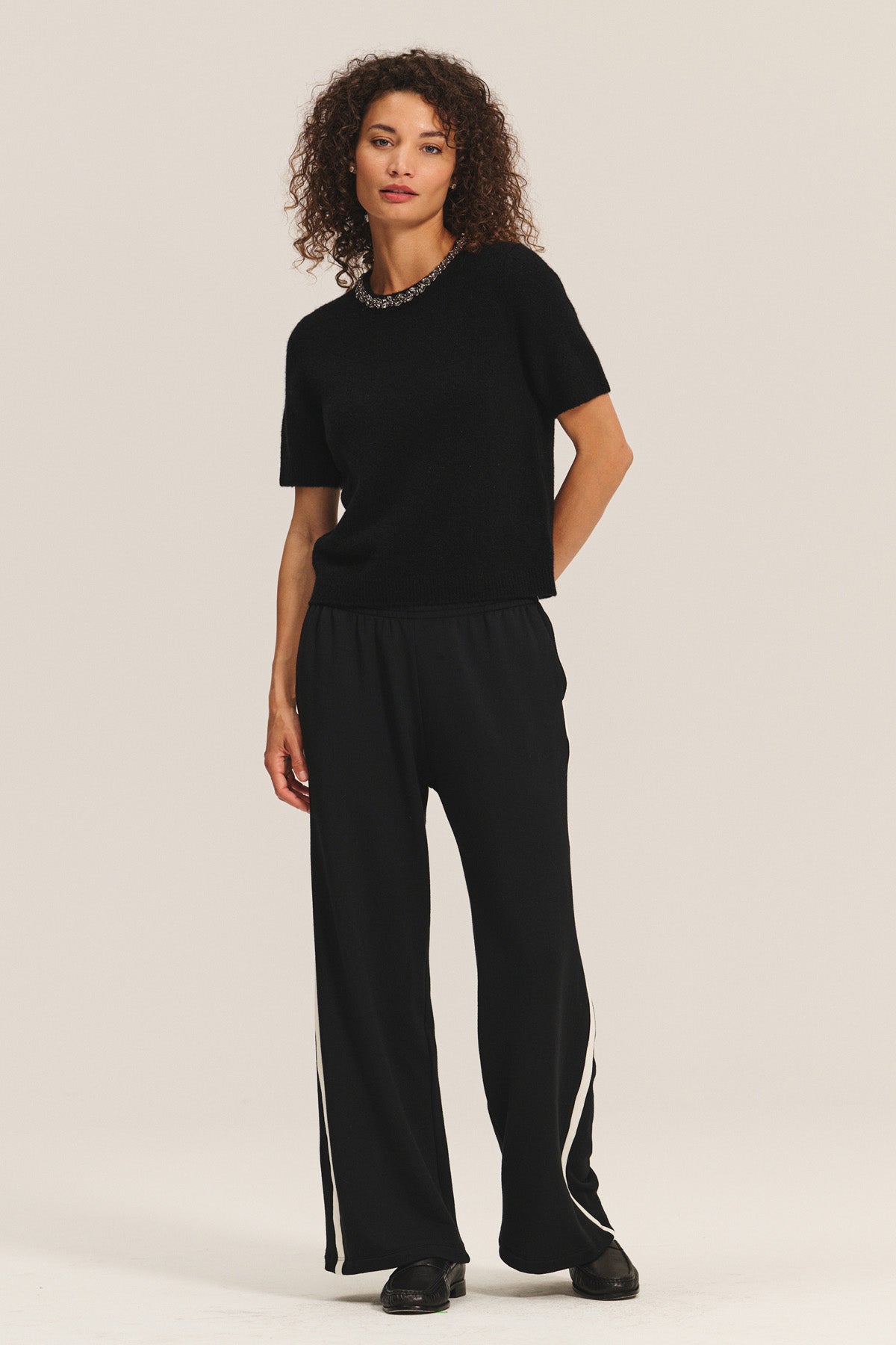 A woman wears the BRIANA SWEATER by Velvet by Graham & Spencer paired with loose black pants with white stripes and black shoes, set against a plain light background—ideal inspiration for your cold-weather wardrobe refresh.