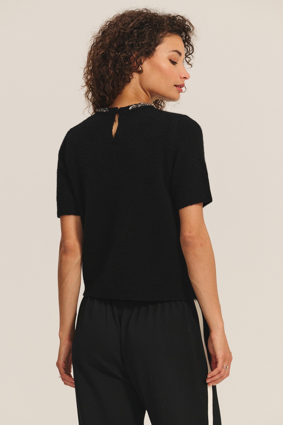 A person is seen from the back wearing the Velvet by Graham & Spencer BRIANA SWEATER in black, featuring a wool blend and a small keyhole opening at the upper back, paired with black pants—ideal for cold-weather style.-40263647723713